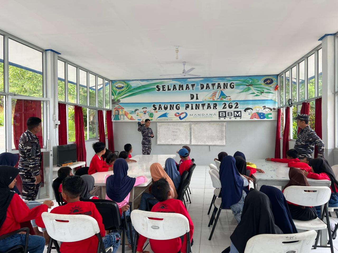 Prajurit KRI Bung Tomo-357 terlihat sedang asik mengajar dan berinteraksi dengan anak-anak di Saung Pintar Sabang Mawang,menciptakan momen belajar yang penuh semangat dan keceriaan.